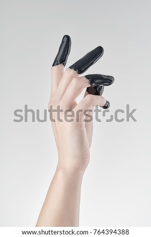 Elegant female hand, fingers dipped in black paint or latex on a light background.