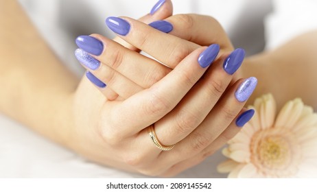 Elegant female hands with fresh violet manicure lying on a white towel next to an gerbera daisy flower. Spa or wellness card. Trendy color 2022 Very Peri
