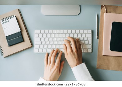 Elegant female hands typing on a computer keyboard, top view of a modern workplace.