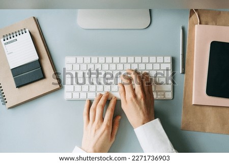 Elegant female hands typing on a computer keyboard, top view of a modern workplace.