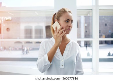 Elegant Female Proud CEO Having Serious Telephone Conversation While Standing In Office Interior, Professional Woman Employee Talking On Mobile Phone With Dissatisfied Boss After Meeting With Clients