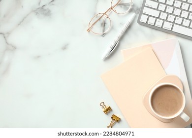 Elegant feminine workspace with paper notebooks, cup of coffee, keyboard, glasses on marble background. Stylish home office desk table. Top view. Flat lay.
