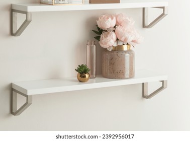 Elegant Floating Shelves Display: A Chic Ceramic Vase with Blush Pink Peonies, a Petite Glass Bottle, and a Small Gold Pot with a Succulent, Creating a Serene and Stylish Wall Accent in a Modern Home. - Powered by Shutterstock