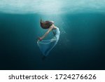 Elegant girl dancer in white dress in a state of levitation under the deep waters of the ocean with sunlight beaming on her face. 