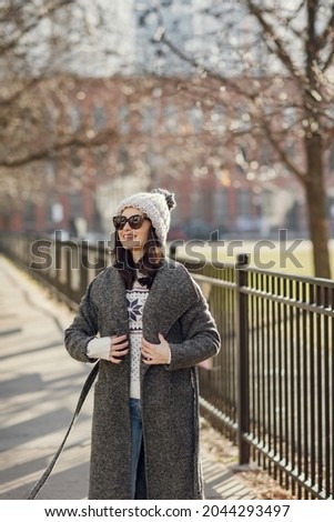Elegant girl walk in a winter city. Woman in a white knited sweater. Beautiful lady with dark hair.