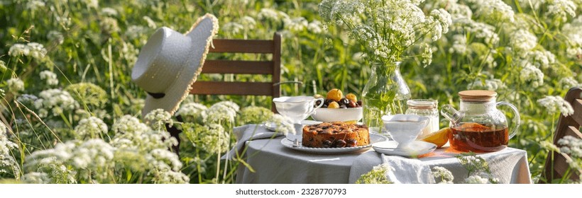 Elegant glamour table setting outdoor in the garden. White porcelain cups, teapot with herbal tea, homemade cherry sweet pie. Family tradition, beautiful place outside. Flower meadow, candles. Banner - Powered by Shutterstock