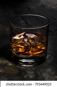 Elegant glass of whiskey with ice cubes on stone background