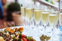 Elegant Glasses With Chilled Champagne Stand In Row Next To Canapes And Snacks On Picturesque Background. Party And Holiday Away. Picnic.