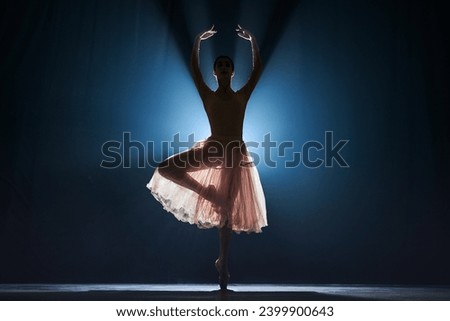Elegant, graceful, slim female dancer, ballerina dancing over dark blue background with spotlight. Silhouette. Concept of art, classical ballet, creativity, choreography, beauty, ad