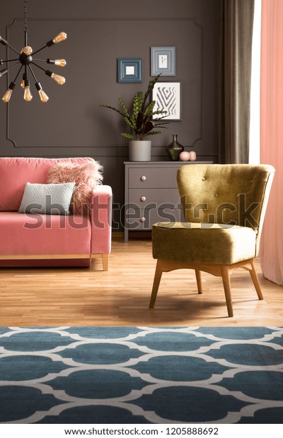 Elegant green armchair and a blue rug with pattern\
on hardwood floor in a dark gray living room interior with a powder\
pink sofa. Real photo.