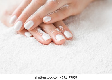 Elegant groomed woman's hands with white nails on the snow. Cares about clean, beautiful, soft hands skin and nails in winter time. Manicure beauty salon. Healthcare concept.