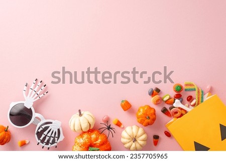 Elegant Halloween trick-or-treat concept. Top view showcasing thematic elements: mini pumpkins, bone, bag with candy corn, sweets, spider, party glasses on light pink backdrop. Room for greeting or ad