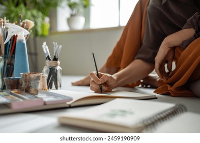 Elegant hand of female painter drawing with brush. Professional woman artist painting watercolor on paper in sketchbook. Creative process at home in daylight, woman making creating paintings sketches - Powered by Shutterstock