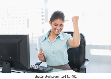 Elegant and happy businesswoman clenching fist in front of computer in a bright office