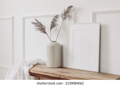 Elegant home interior decor still life photo. Vase with dry reed, grass on old wooden bench. Blank white picture frame mockup. Wall moulding background, trim decor. Empty copy space. Side view.  - Shutterstock ID 2130084062