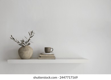 Elegant home still life. Floating shelf. Textured vase with green olive tree branches, old books. Cup of coffee, tea. Modern Mediterranean appartement. White wall background, interior indoor mockup - Powered by Shutterstock