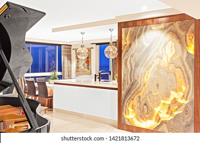 An elegant house interior showcasing a grand piano, a mural, and kitchen and dining space at the background