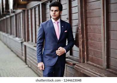 Elegant indian macho man model on suit and pink tie posed against wooden stalls. - Shutterstock ID 1244623048