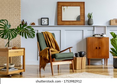 Elegant interior of home room with design armchair, retro furniture, wooden mirror, shelf, tropical leaf,  plant, decoration, carpet and persnoal accessories in stylish home decor.