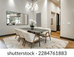 Elegant interior image of a dining room with black steel table soft tone curved back chairs swirling light fixture orchid and area rug contemporary home