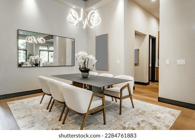 Elegant interior image of a dining room with black steel table soft tone curved back chairs swirling light fixture orchid and area rug contemporary home