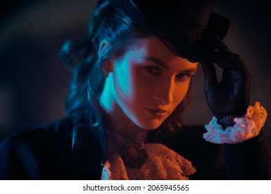 An elegant lady in a 19th century suit against a dark background in mixed color light. Historical hairstyle and makeup.