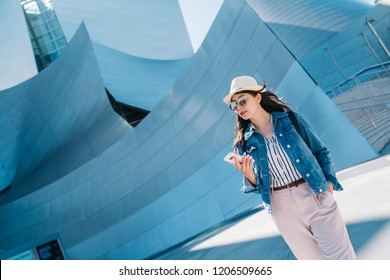 elegant lady walking around Walt Disney concert hall with cellphone in her hand. popular sightseeing spot to visit in Los Angeles. young tourist using online tour guide on smartphone.