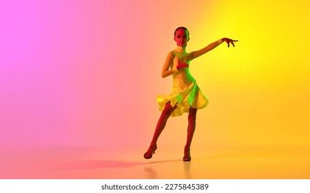 Elegant little girl in adorable stage outfit  dress dancing ballroom dance over gradient pink  yellow background in neon light filter  Concept beauty  professional dances  skills  Emotions in dance