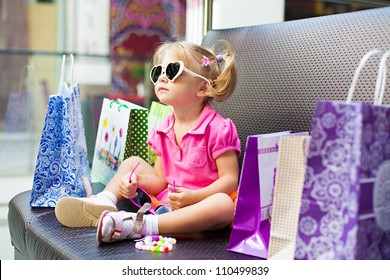 Elegant little girl posing on a big sofa in the mall on the background shop windows.