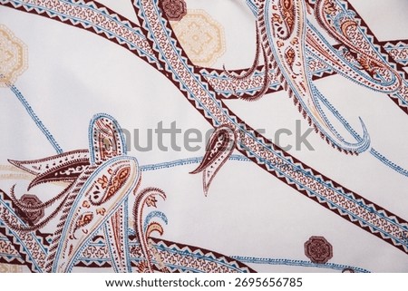 Elegant and luxurious fabric pattern featuring classic brown and blue paisley motifs interwoven with decorative chains and medallions on a bright white background. Ideal for fashion, silk, or vintage 
