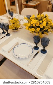 An elegant, luxurious table setting featuring a rich yellow rose centerpiece, tall white candles in a silver candelabra.