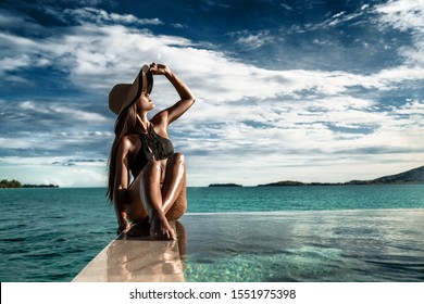 Elegant luxury black swimsuit swimwear model woman with sun hat on infinity pool resort vacation. Europe holiday hotel for wellness spa, hair removal laser legs and body care.