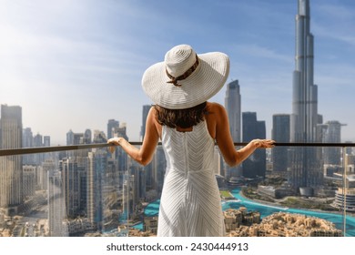 A elegant luxury woman with a white hat enjoys the view over the Downtown City skyline of Dubai, UAE - Powered by Shutterstock