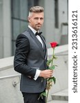 elegant man in black tux. man wearing tux bowtie outdoor. adult tux man with red rose