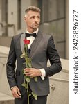 elegant man in black tux. man wearing tux bowtie outdoor. grizzled tux man with red rose