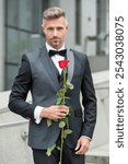 elegant man in black tux. man wearing tux bowtie outdoor. luxury tux man with red rose