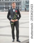 elegant man in black tux. man wearing tux bowtie outdoor. tux man with red rose. full length.