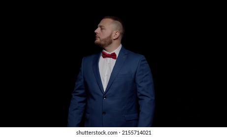 An Elegant Man In A Blue Tuxedo With A Red Tie On A Black Background, Looks Up And Then Forward.