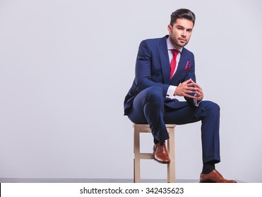 Elegant Man In Business Suit Sitting In Studio With Palms Touching While Resting His Leg On Chair