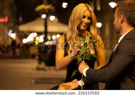 An elegant man giving his date a red rose