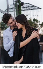 Elegant Man Hugging Cheerful Woman In Black Blazer