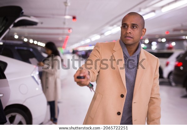 Elegant man opens car with car alarm keychain in\
underground parking