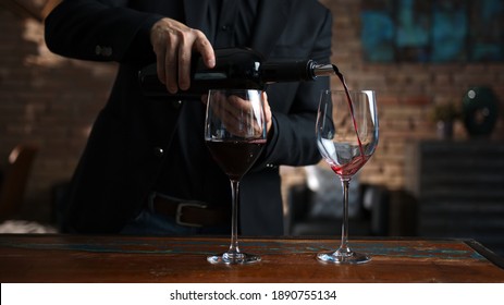 Elegant man pouring red wine from wine bottle to wine glasses at home in a cosy dark room. - Powered by Shutterstock