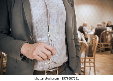 Elegant man in a social event, man with glass of wine or  champagne (in the background blurred people sit together at lunch)