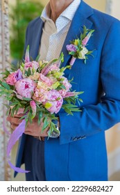 Elegant man in a suit holds a round bouquet with peonies and eustoma.Boutonniere of eremurus, white eustoma and greenery attached to grooms blue jacket. Wedding details and floristics - Shutterstock ID 2229682427