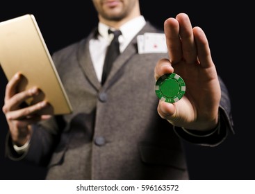 Elegant Man In Suit No Face, Holding Green Poker Chip And Tablet In Hands, Cards In Pocket/ Internet Gambling, Dark Background 