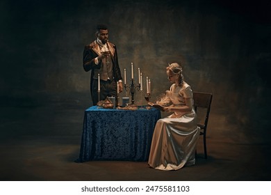 Elegant man in vintage attire holds a wine glass next to table with candles, woman in satin dress reading book. Dimly lit, historical background. History, retro and vintage, comparison of eras concept - Powered by Shutterstock