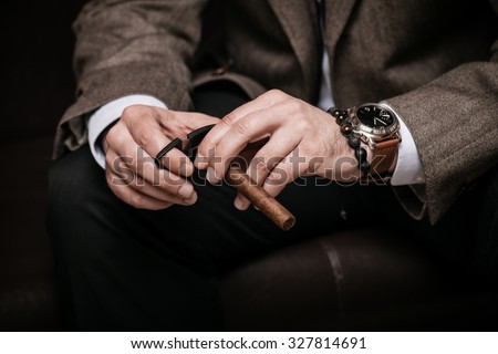 elegant man wearing suit and white shirt cut Cuban cigar indoor shot, closeup, selective focus