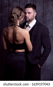 An elegant man and woman look at each other affectionately, while the girl adjusts the man's tie.