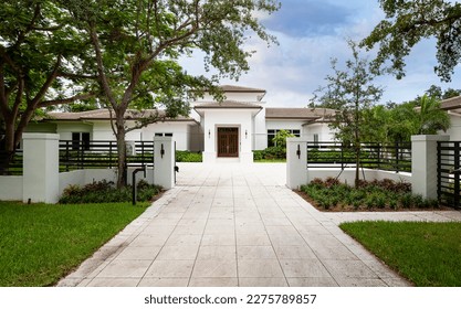 Elegant mansion entrance located in the Pinecrest village, in Miami-Dade, Florida, with large tropical vegetation around it, short grass, driveway, summer weather, trees, palm trees, blue sky - Powered by Shutterstock